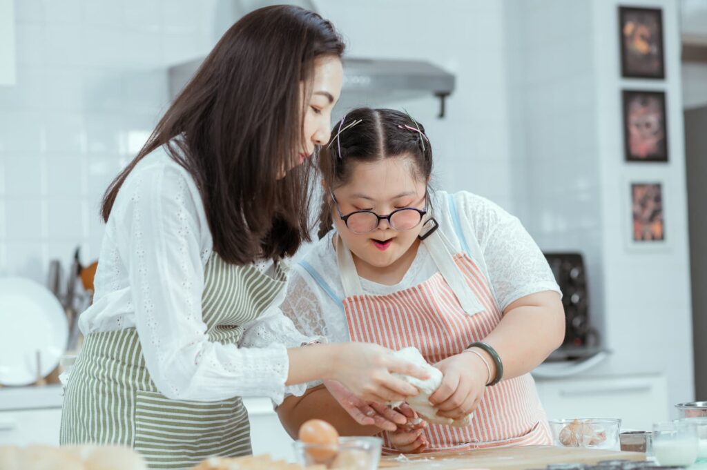 Persona voluntaria ajudant a la cuina a una noia amb síndrome de Down